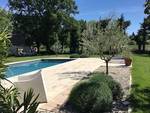 Une piscine dotée d’une terrasse carrelée, entourée de verdure et d’arbres.