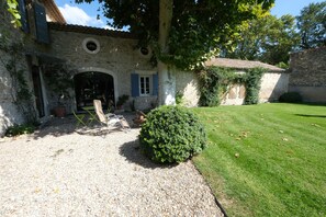 Un bâtiment en pierre avec une allée en gravier, un petit arbuste et une pelouse.