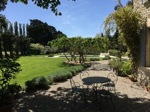 Un jardin avec un chemin de gravier, une table entourée de chaises et un bâtiment situé sur la droite.
