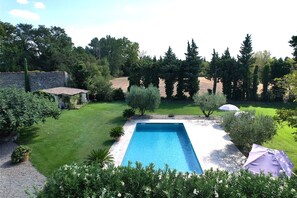 Una piscina rectangular rodeada por un césped cuidado, con un muro de piedra y árboles al fondo.