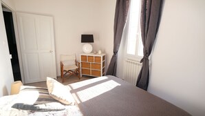 Un dormitorio con cama, una silla, cómoda y ventana con cortinas.