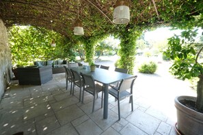 Un patio al aire libre con mesa y sillas, rodeado de follaje y una pérgola.