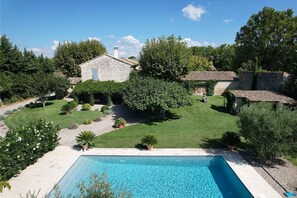 Vue sur une propriété depuis la piscine, avec une maison en pierre, une pelouse bien entretenue et une piscine à l’eau d’un bleu limpide.