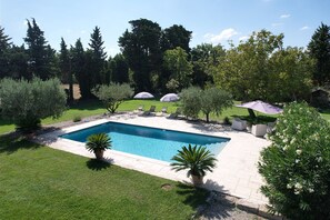 A rectangular swimming pool with a tiled deck, surrounded by a well-maintained lawn and various trees.