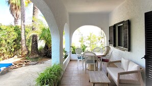 Un área de patio techada con una mesa y sillas, rodeada de arcos y plantas en macetas.
