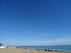 A beach with a clear sky, a few people, and a boat in the distance.