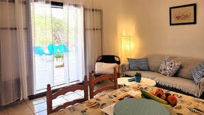 Una sala de estar con un sofá, una silla de madera, una mesa con mantel individual, una lámpara y una ventana con cortinas.