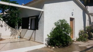 Un edificio blanco con techo de tejas, un pequeño porche con puerta y un aplique de pared.