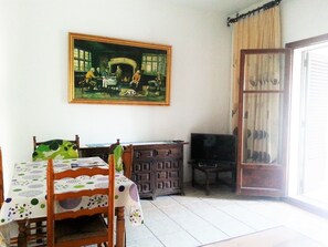 A dining area with a table set for four, a television on a stand, and a painting above the table.