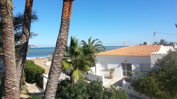 Vista costera con palmeras, una playa y un edificio blanco con techo de tejas.