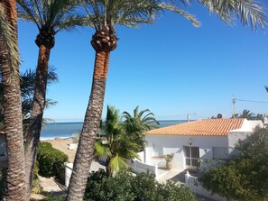 A coastal view with palm trees, a beach, and a white building with a tiled roof.