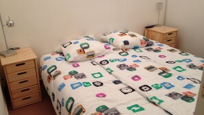 A bedroom with a bed covered in a white duvet with colorful icons, two bedside tables, and a lamp on one table. - AJACCIO Furnished apartment with breathtaking sea view, facing Marinella beach. (Ajaccio)