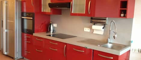 A modern kitchen with red cabinets, stainless steel appliances, and a white countertop.
