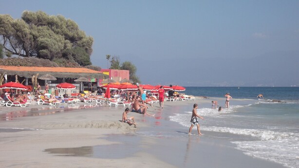 A beach with sun loungers, umbrellas, and people enjoying the water. - AJACCIO Furnished apartment with breathtaking sea view, facing Marinella beach. (Ajaccio)