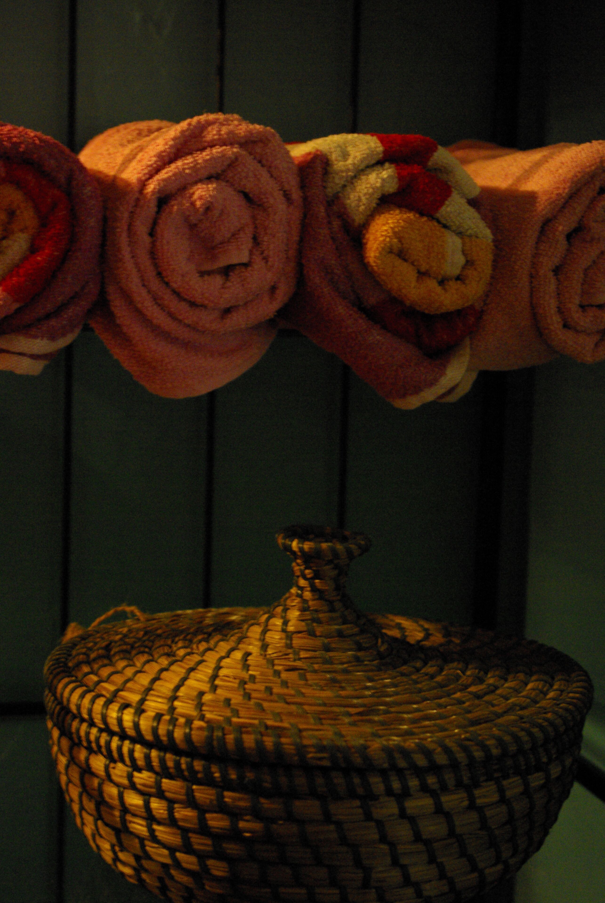 A set of rolled towels in various colors, a woven basket, and a dark wooden background.