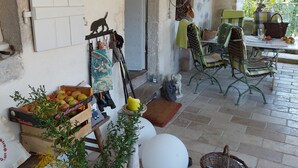 A rustic outdoor seating area with a table, chairs, and a variety of items including a basket, a potted plant, and a crate of apples.