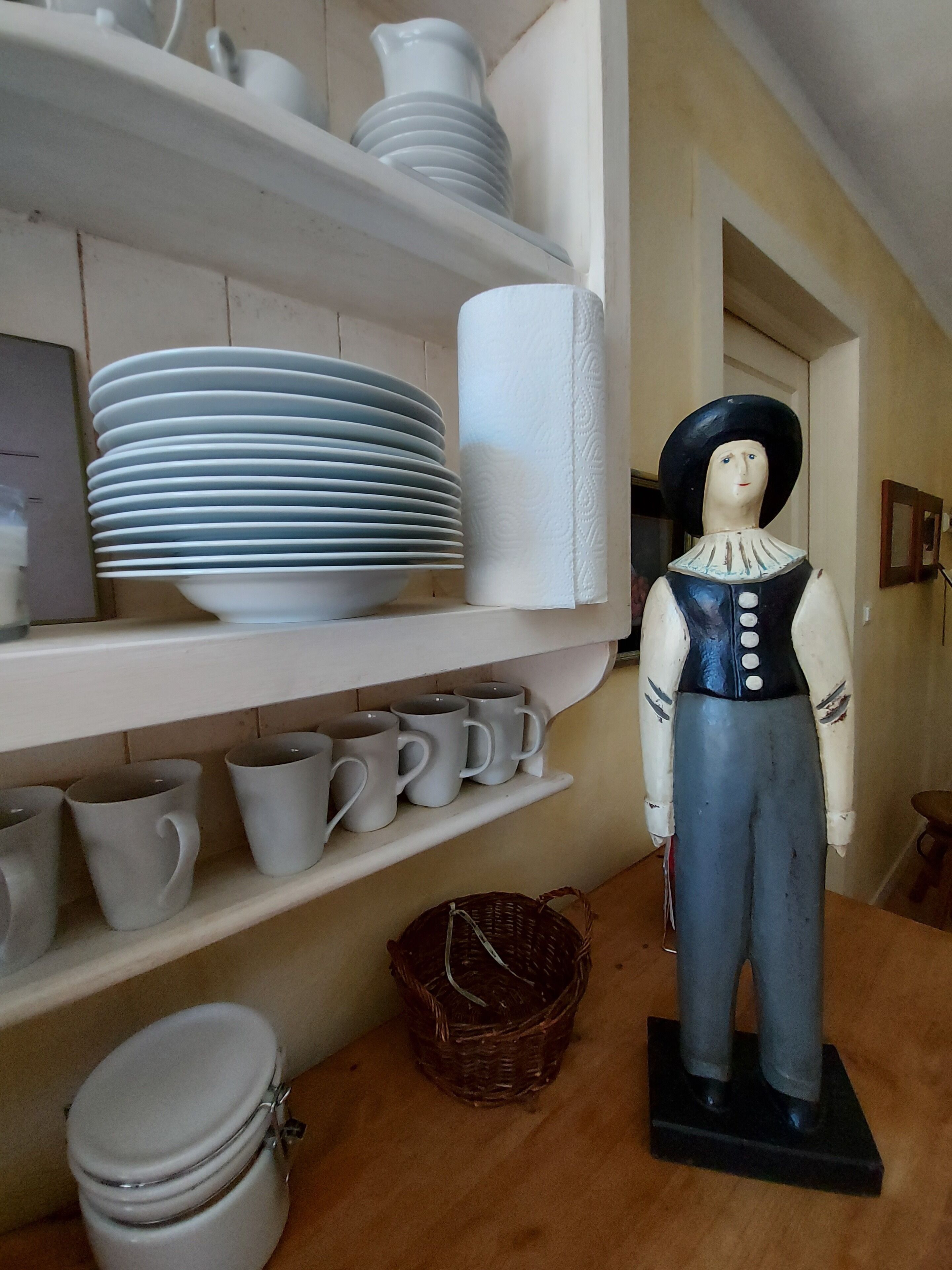 A room with shelves holding plates, mugs, and a wicker basket.