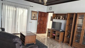 Una sala de estar con un sofá, un mueble de madera con puertas de cristal, un televisor y una puerta con marco de madera.