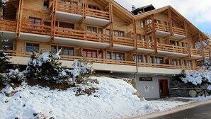 A multi-story wooden building with balconies, a stone wall entrance, and snow-covered surroundings. - Charming apartment facing south, overlooking the Cervin. Val d'Anniviers (Saint-Luc)
