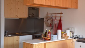 A kitchen with wooden cabinets, a stainless steel sink, an oven, and a coffee maker. - Charming apartment facing south, overlooking the Cervin. Val d'Anniviers (Saint-Luc)