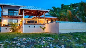 A modern house with a large patio, a covered outdoor area, and a view of palm trees. - Vivaro South House Luxury Villa Private Infinity Pool (West End)