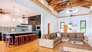 A spacious living area with a large sectional sofa, a kitchen with modern appliances, and a high ceiling with exposed beams. - Vivaro South House Luxury Villa Private Infinity Pool (West End)