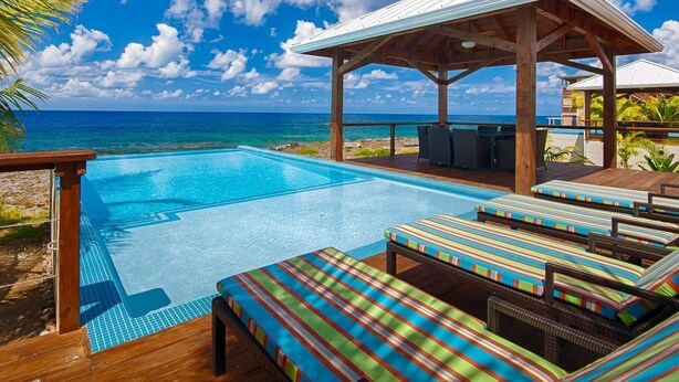 A pool area with lounge chairs and a covered seating area, overlooking a beach and ocean. - Vivaro South House Luxury Villa Private Infinity Pool (West End)