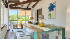 A spacious room with a wooden dining table, a bench, and a view of a swimming pool. - Beautiful villa with pool and garden,a/c, quiet location,  beach 200 mt (Cala Serena)