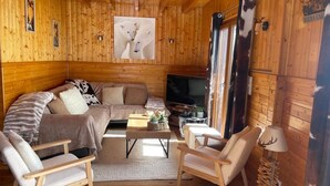 A cozy cabin interior with a wooden interior, a sofa, two chairs, a coffee table, a TV, and a large window. - La Clusaz skiing and biking (La Clusaz)