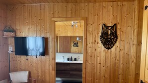 A wooden-paneled room with a bed, a chair, a TV, a bathroom with a sink and mirror, and a decorative wall piece. - La Clusaz skiing and biking (La Clusaz)