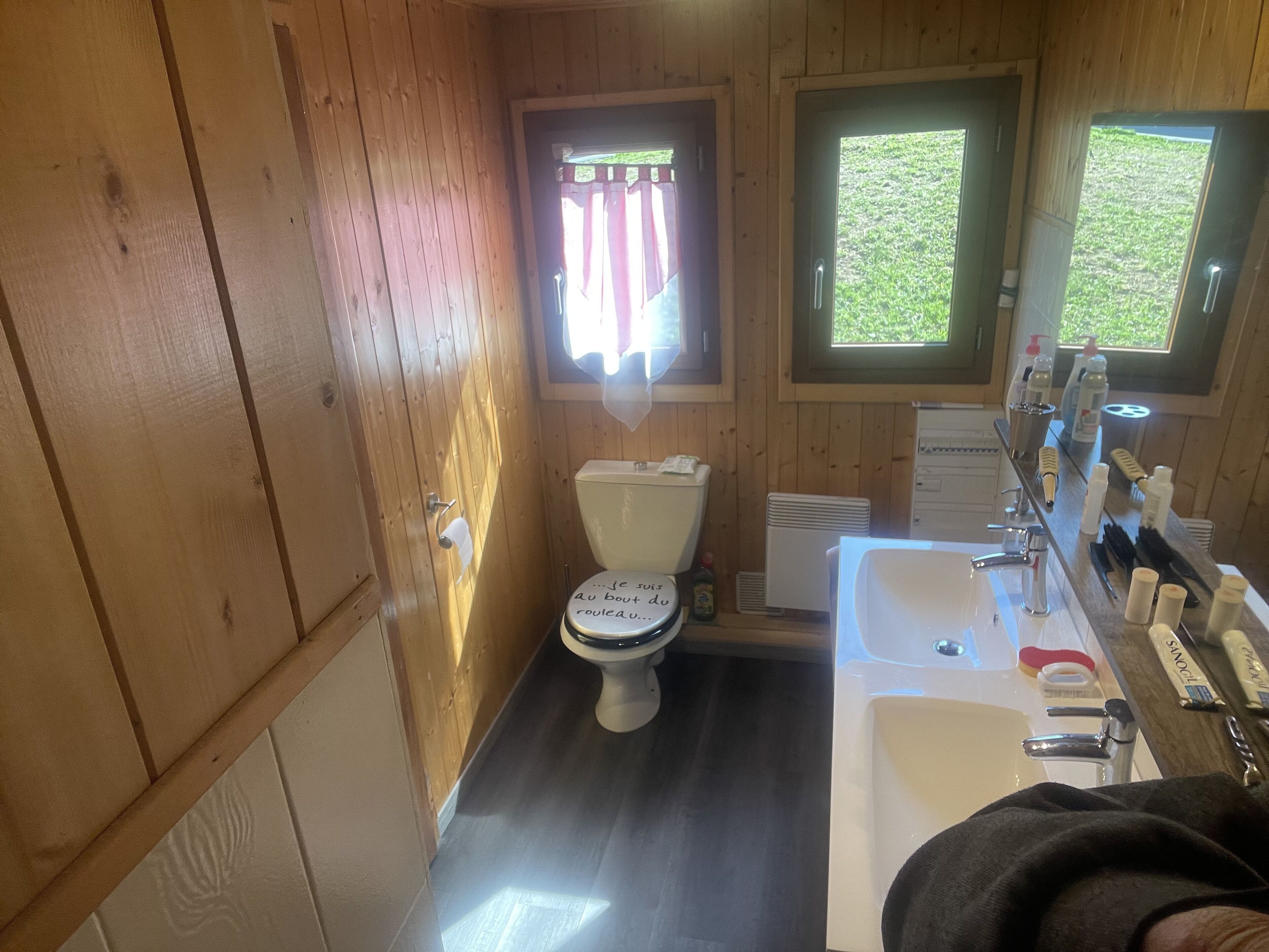 A wooden cabin bathroom with a toilet, sink, and window.