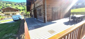 A wooden deck with outdoor furniture, a vehicle, and a building with a balcony.