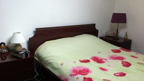 A hotel room with a single bed, a nightstand with a lamp, a remote control, and a decorative item.
