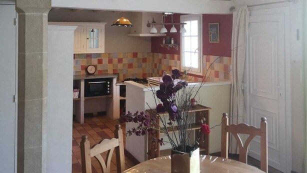 A dining area with a stone wall, a kitchen in the background, and a view of the outside.