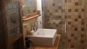 A bathroom with a wooden vanity, a sink, a mirror, and a shower with mosaic tiles.