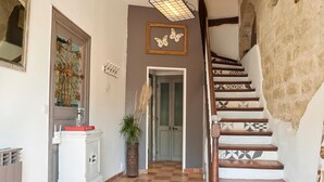 A hallway with a checkered floor, a staircase with patterned tiles, a white cabinet with a red object on top, and a door with a butterfly decoration above it.