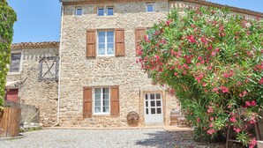 A stone building with wooden shutters, a gravel driveway, and a flowering tree.