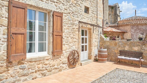 A stone building with wooden shutters, a white door, and a rustic bench.