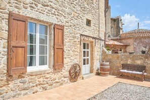 Un bâtiment en pierre avec des volets en bois, une porte blanche et un banc rustique.