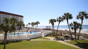 A pool area with a view of the beach and ocean, surrounded by palm trees and a white fence. - El Matador 428 - FREE TICKETS!! Your stay includes free tickets to many area attractions! (Fort Walton Beach)