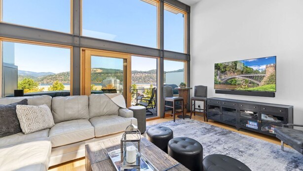 A modern living room with a large window, a sofa, a coffee table, and a flat-screen TV mounted on the wall. - River Views! Contemporary Condo Centrally Located Walk To Restaurants/Breweries (Hood River)
