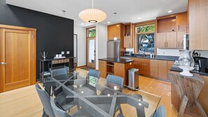 A modern kitchen with wooden cabinets, a stainless steel refrigerator, and a glass dining table with chairs. - River Views! Contemporary Condo Centrally Located Walk To Restaurants/Breweries (Hood River)