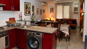 Une cuisine compacte avec un lave-linge intégré, un coin repas avec une table et des chaises, et un salon avec un canapé et un téléviseur.
