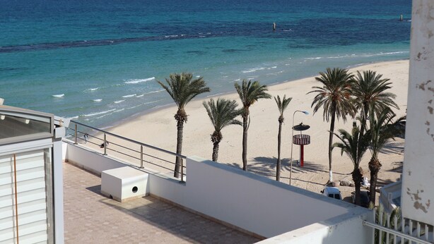 Une vue sur la plage depuis un balcon, avec des palmiers et une plage de sable.