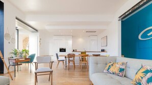 A modern living room with a grey sofa, wooden chairs, and a dining area with a table and chairs.