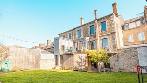A two-story stone building with a balcony, a wooden fence, and a grassy yard.