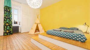 A room with a yellow wall, a bed with patterned bedding, a tent, and a window with curtains.