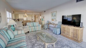 Una sala de estar con un sofá, sillones, una mesa de centro de vidrio, un televisor y un mueble.