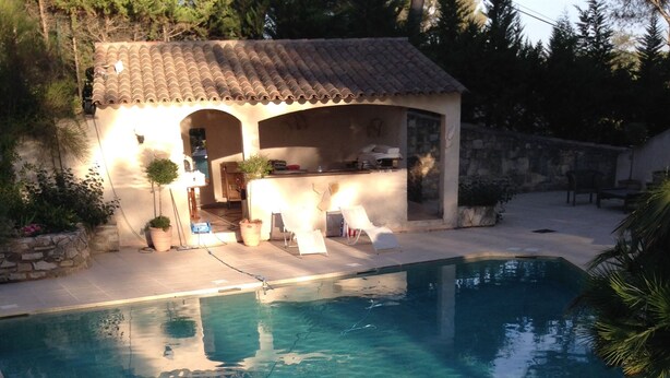 Une piscine aux eaux cristallines, entourée d’une terrasse carrelée et bordée d’un petit bâtiment dont le toit est également recouvert de tuiles.