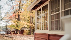 A building with large windows and a wooden exterior, surrounded by trees with autumn foliage. - Relax in Bayview Cabin MW Chain, June Opening (Manitowish Waters)